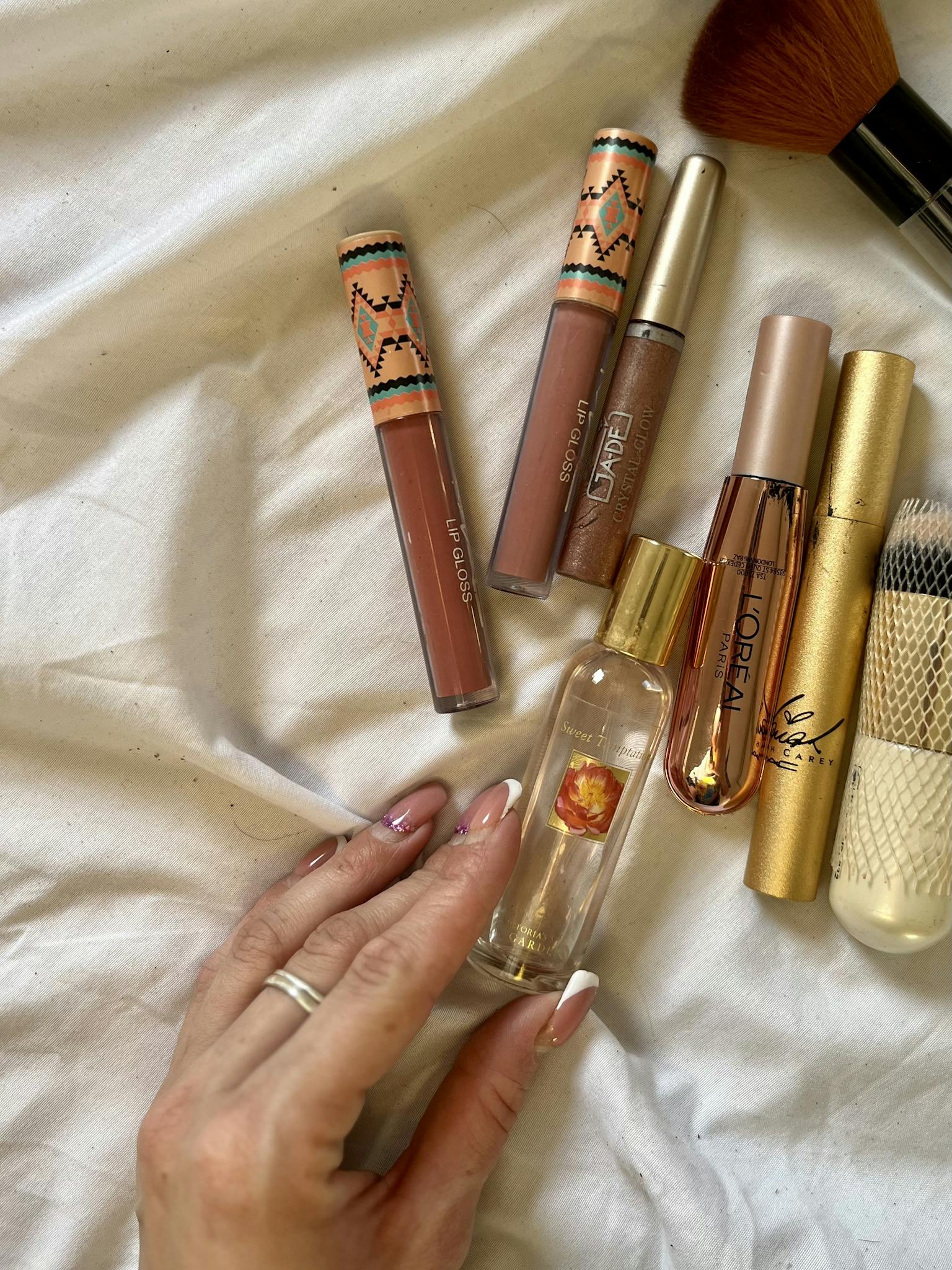 A stylish flat lay of cosmetics including lip gloss, mascara, and a hand holding a perfume bottle.